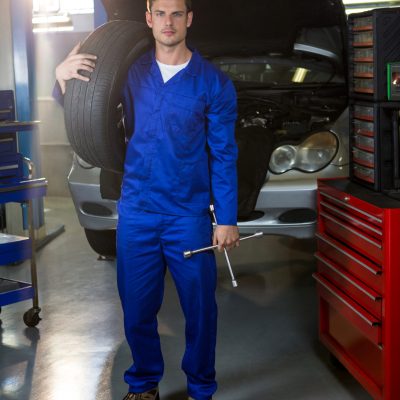 Portrait of mechanic holding tyre and lung wrench at repair garage